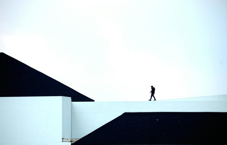 Silhouette of a person walking on a geometric architectural structure under a vast sky.